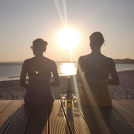 2 Frauen sitzen am Meer beim Sonnenuntergang