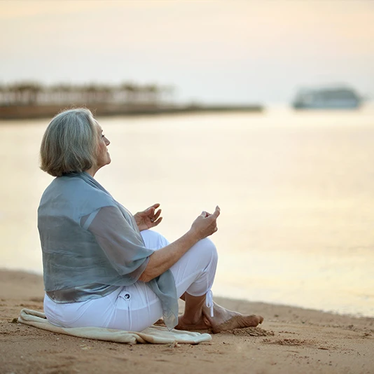 Frau mit grauen Haaren sitzt am Meer